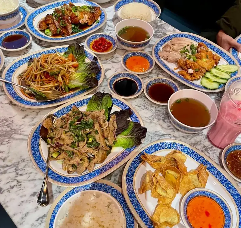 A table of nam tok, som tum, crispy wontons, roast duck and chicken on blue and white plates
