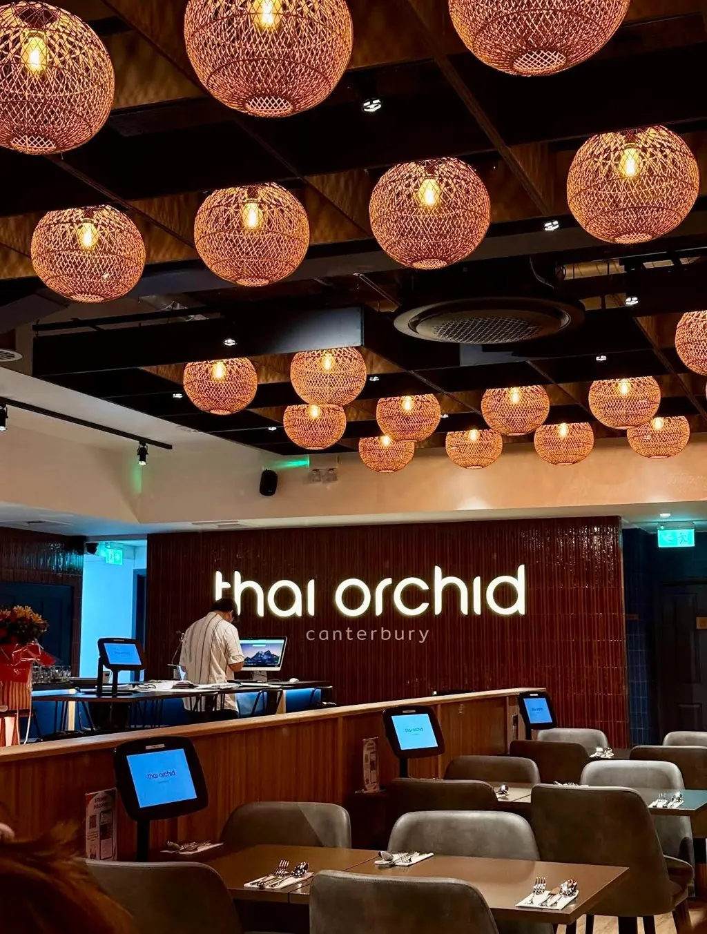 The Thai Orchid dining room: woven rattan lanterns, a tiled walnut wall and the lit sign